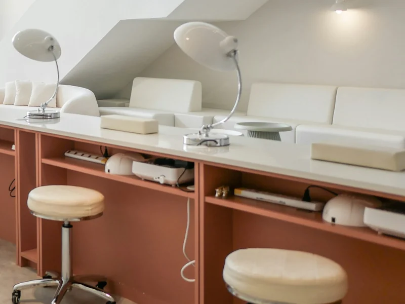 Meja manicure putih dengan lampu meja dan kursi bundar di studio kuku