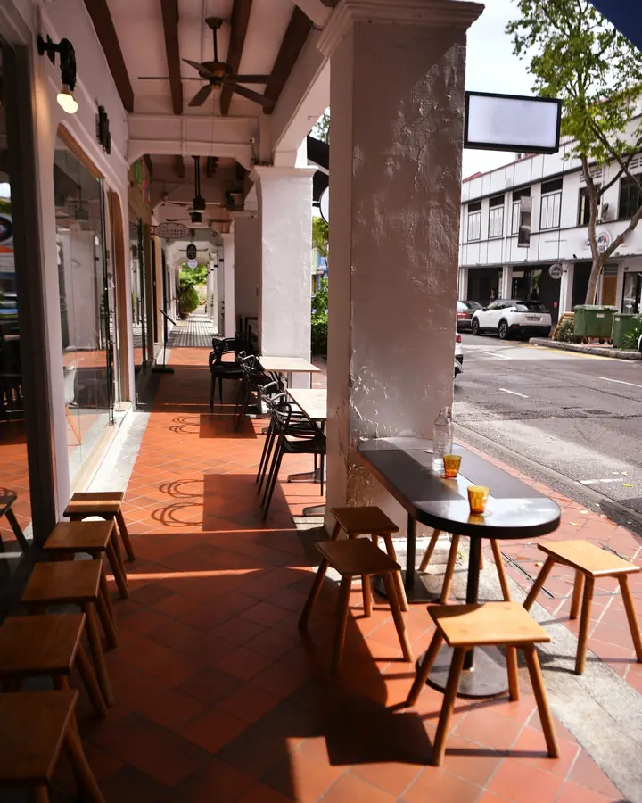 Café tables and stools along a shophouse five-foot way with terracotta floor tiles