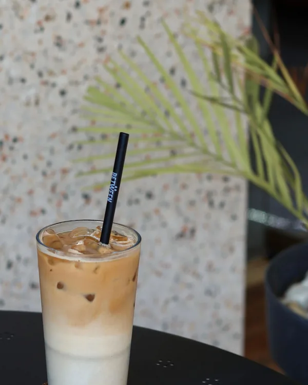 Iced latte in a glass with a black straw against a terrazzo wall
