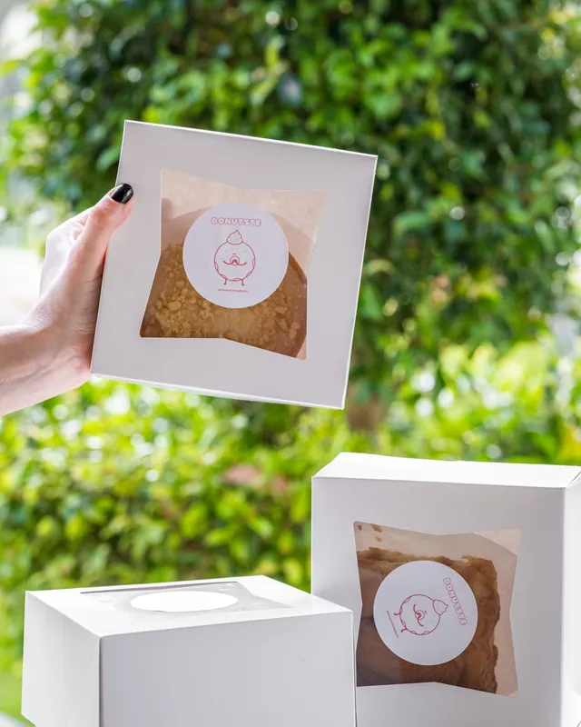 Hand holding a white window cake box, with more boxes on a table outdoors