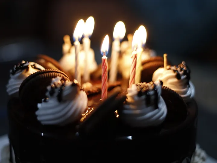 Chocolate cake topped with cream swirls and lit birthday candles