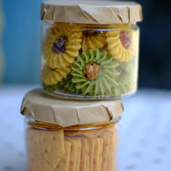 Two cookie tubs with brown paper lids, flower-shaped butter cookies on top