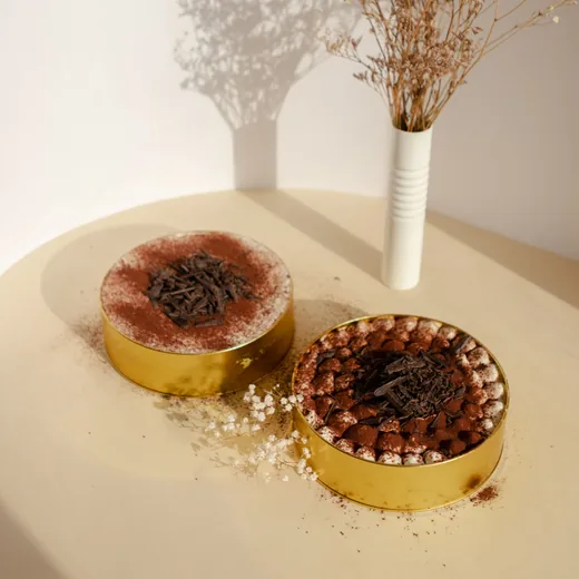 Two small cocoa-dusted cakes beside dried flowers