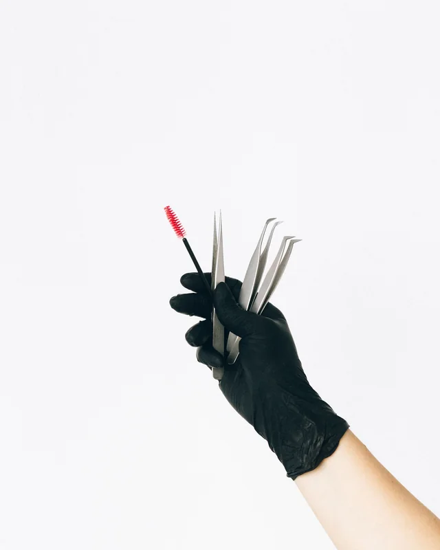 Gloved hand holding sterilised lash tweezers and a fresh spoolie