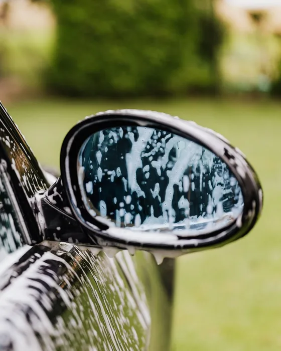 Thick foam pre-soak running down a dark car's side mirror and door