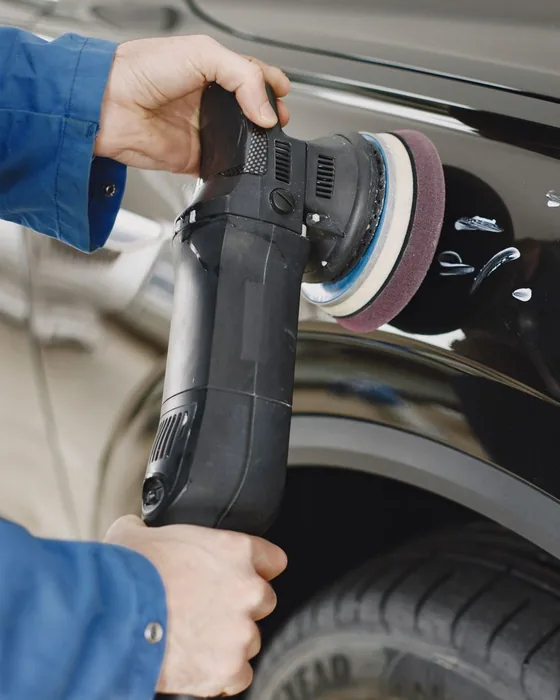 Hands guiding a dual-action polisher across a black car's front fender