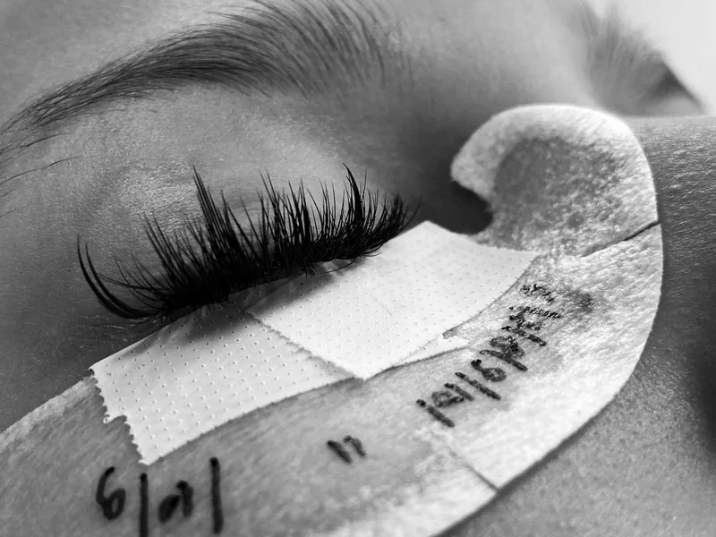 Black and white close-up of fresh eyelash extensions, under-eye pad taped in place