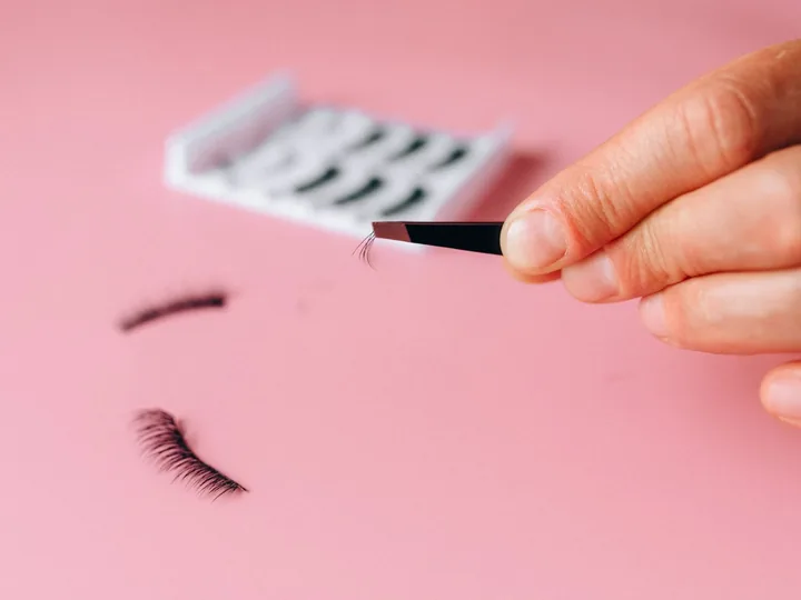 Lash tweezers picking a single extension from a tray on pink